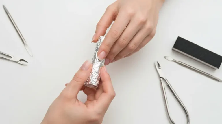 Kobieta owijająca palce folią aluminiową do usuwania hybryd acetonem - paznokcie z błyszczącą hybrydą